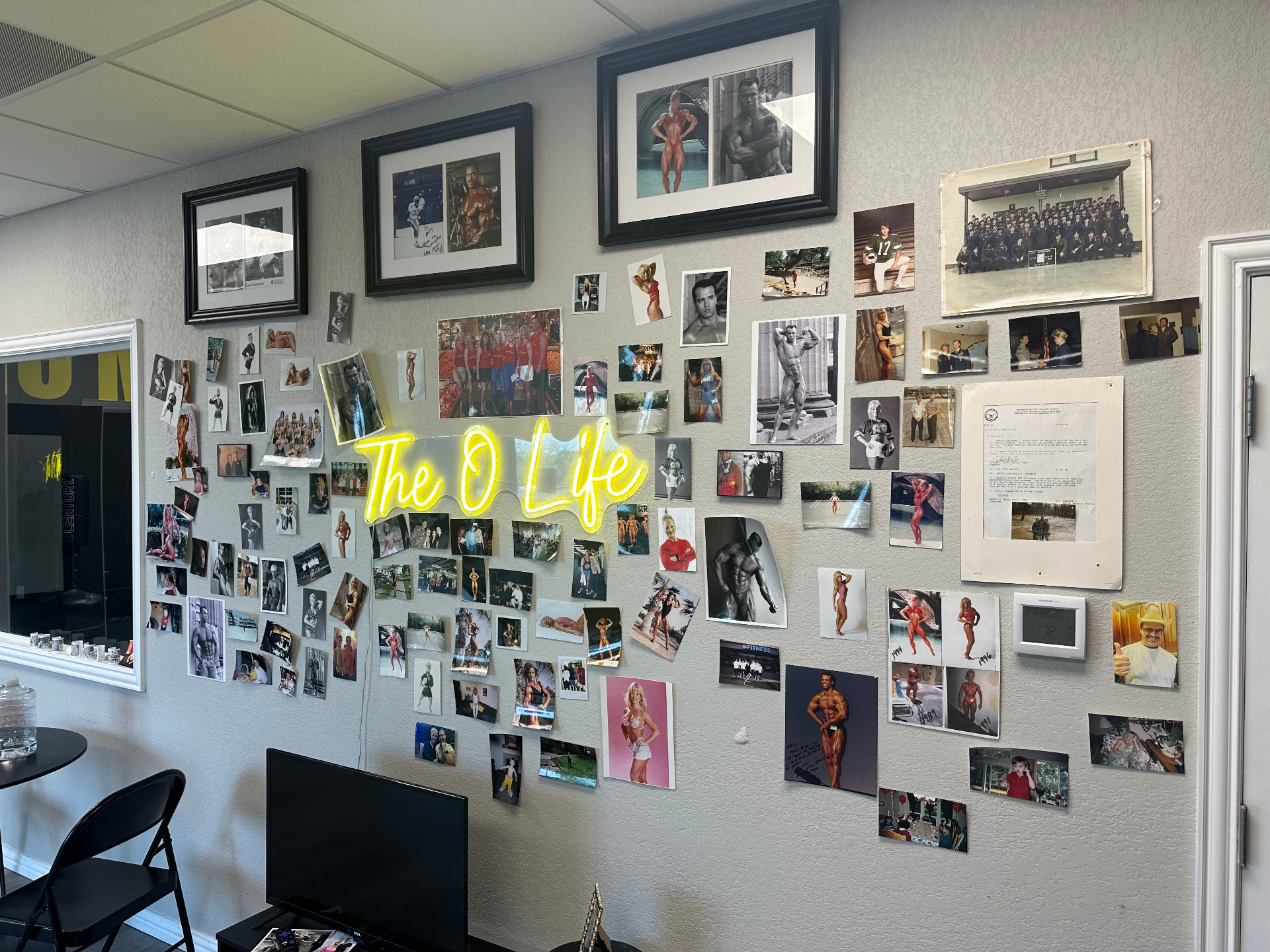 The O Life Legacy Wall covered with signed photos, memorabilia, and a glowing yellow The O Life neon sign at the Little Elm, Texas studio